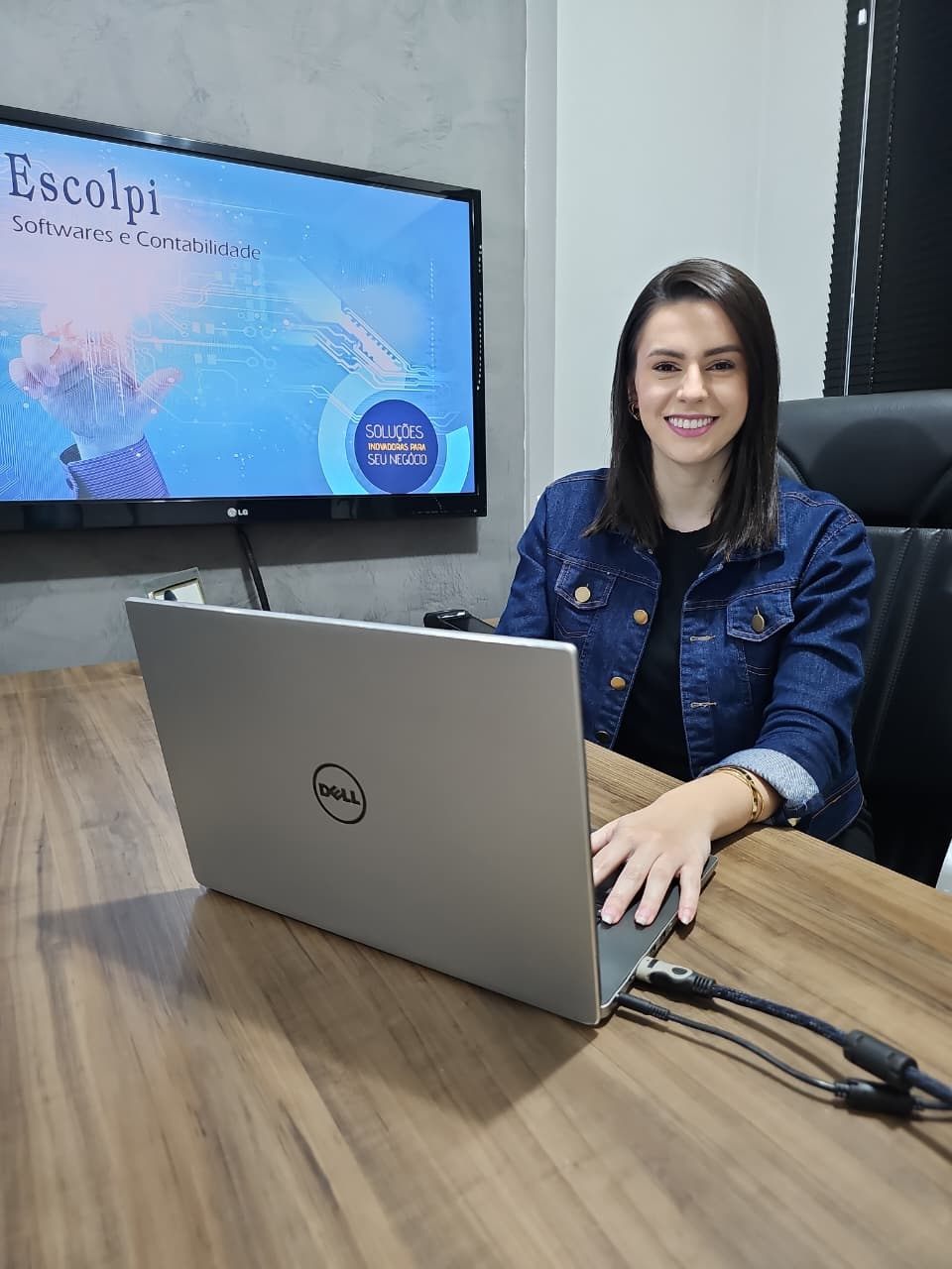 Integrante da equipe Escolpi na sala de reuniões, com a marca Escolpi Softwares e Contabilidade na TV