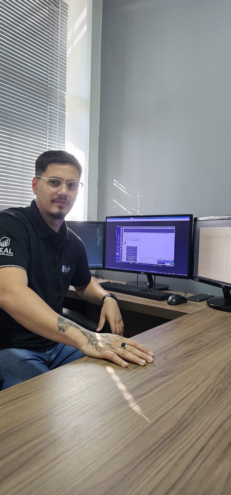Integrante da equipe Escolpi em frente a três monitores com o sistema aberto