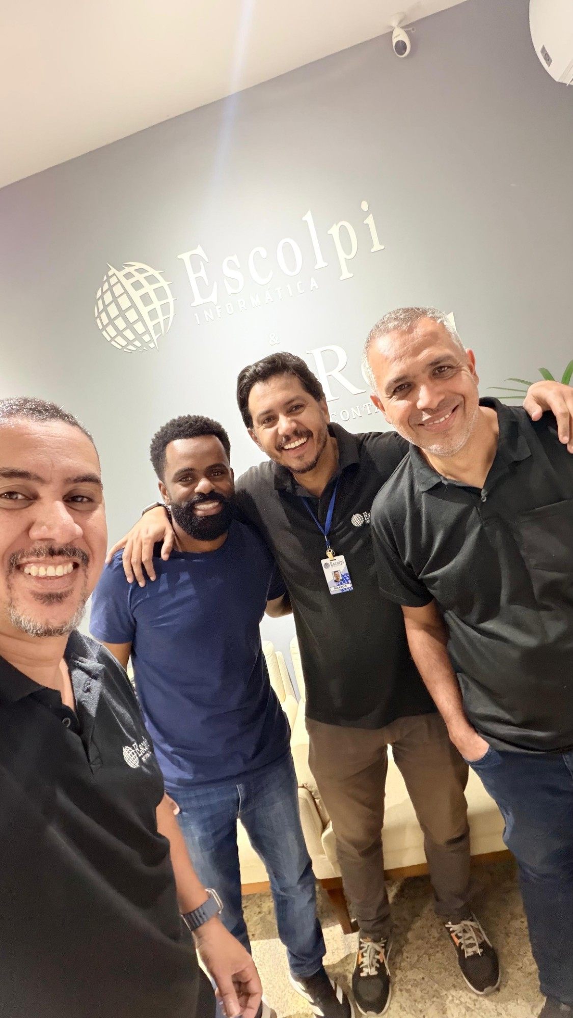 Integrantes da equipe Escolpi abraçados em uma selfie na recepção do escritório