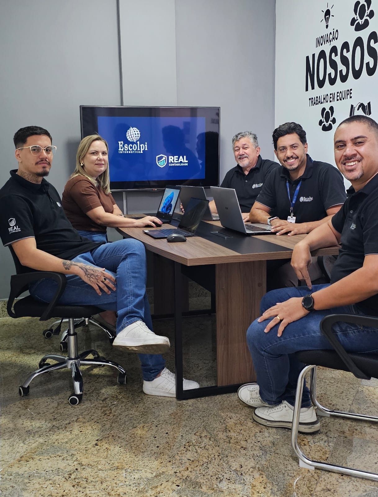 Equipe da Escolpi e da Real Contabilidade BH reunida no escritório, com as duas marcas na TV